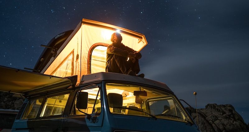 man sitting on top of blue van staring at sky during nighttime